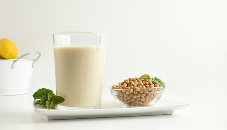Background with soy milk and bowl with seeds on white ceramic plate on white table and leaves. Front view.の写真素材