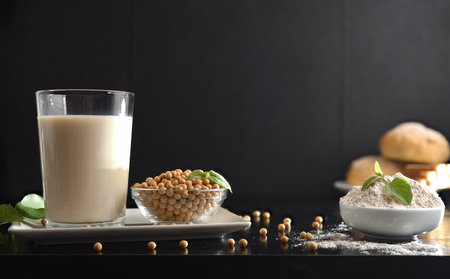 Soy drink and products on black table with soybean seeds and leaves and black isolated background. Front view.の写真素材