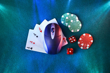 Online casino gaming concept with computer mouse over playing cards in the center with dice and betting chips around on green mat edge-lit. Top view.の写真素材