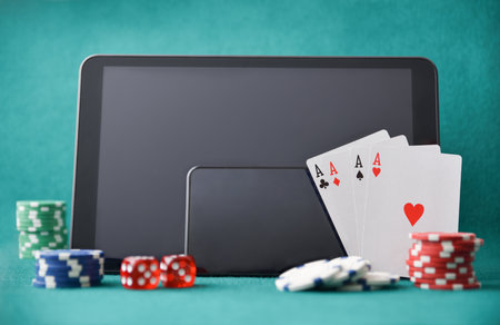 Electronic devices for online casino game on gaming table with chips, cards and dice on felt table and green background. Front view.の写真素材