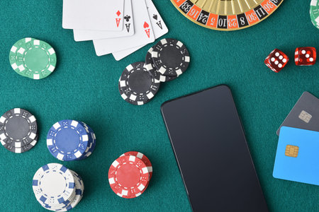 Concept of playing casino games online with smartphone on a game table with green felt full of game...