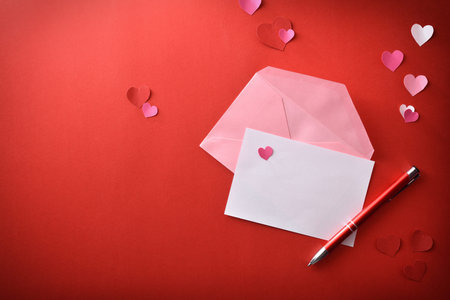 White empty sheet with red pen and open pink envelope on red romantic background with heart cutouts....