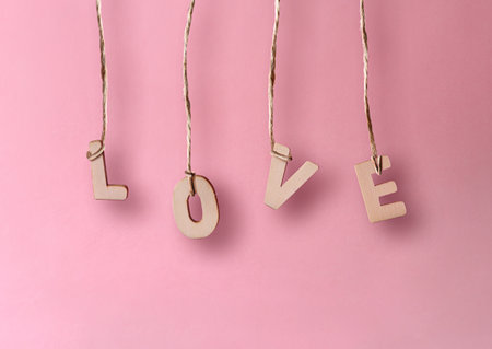 Wooden letters forming the word love held with a jute thread isolated on pink background. Front view.の写真素材
