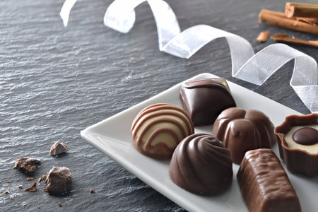 Assortment of chocolate bonbons on white ceramic plate on a slate table with white ribbon and cinnamon sticks. Elevated view.の写真素材