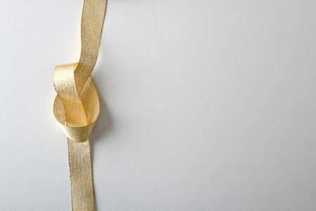 Shiny golden textile ribbon with knot placed on the left side and isolated on white background. Top view.の写真素材
