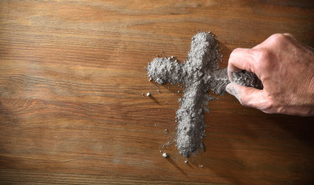 Hand making Christian cross symbol with ashes on wooden table. Top view.の写真素材