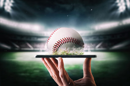 Concept of live online broadcast of baseball championship with hand holding a mobile phone with ball and baseball stadium in the background.の写真素材