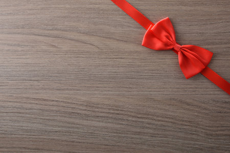 Little red bow with ribbon at the top right for event background decoration on wooden table. Top view.の写真素材