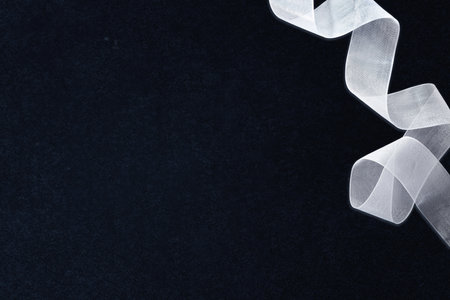 White tulle ribbon with waves in the upper right corner on textured isolated dark background. Top view.の写真素材