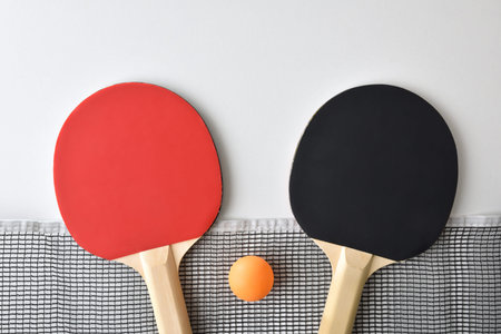 Background with set of table tennis paddles; net and orange ball isolated on white table. Top view.