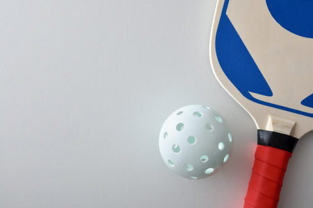 Detail of pickleball racket and a white ball isolated on white table. Top view.