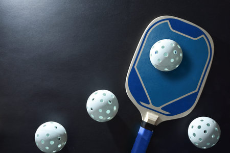 Background with blue wooden pickleball paddle and four white balls on a black table. Top view.