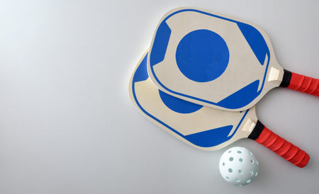 Two pickleball rackets and a white ball isolated on white table. Top view.