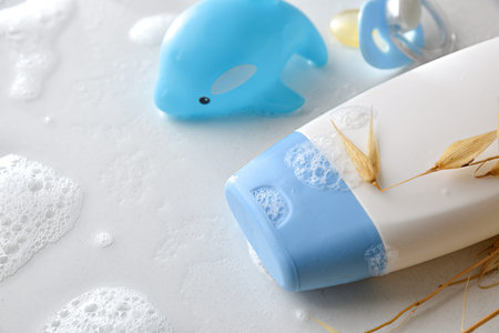 Baby bath concept with detail of soap bottle toy and pacifier on white table wet with water and...