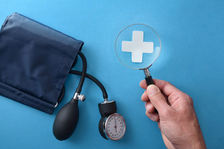Blood pressure diagnosis concept with hand and magnifying glass on medical crus on blue background with blood pressure monitor. top viewの写真素材