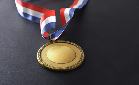 Golden metal medal with blue white and red colors isolated on black background. Elevated view.