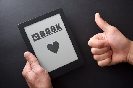 Detail of hand taking an ebook with message and heart written on the screen and hand with ok gesture isolated on black table. top view.の写真素材