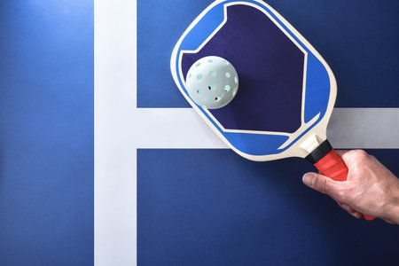 Hand with blue pickleball paddle hitting a white ball on playing surface. Top view.の写真素材