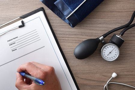 Doctor prescribing medications on a document for blood pressure on a wooden office table with blood...