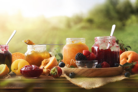 Natural homemade jams of various fruits in jars on a wooden table in the countryside. Front view.の写真素材
