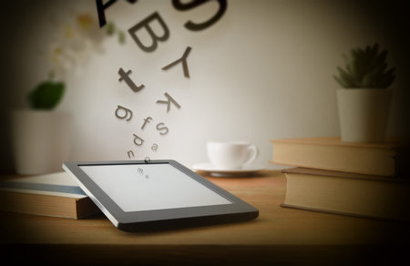 Reading concept with ebook on wooden table at home with letters coming out of the screen and coffee...
