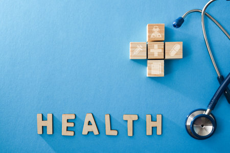 Healthcare background in various fields with wooden cubes screen printed with medicine drawings, cutouts of letters forming the word health and stethoscope. Top view.の写真素材