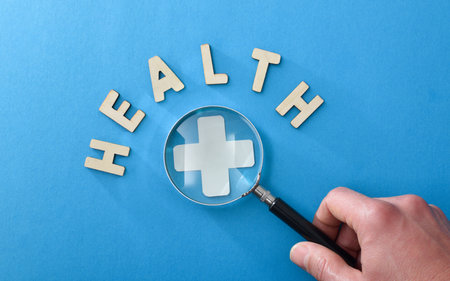 Medical information and examination background with hand magnifying a medical cross with a magnifying glass and letters with health message on blue isolated background. Top view.の写真素材