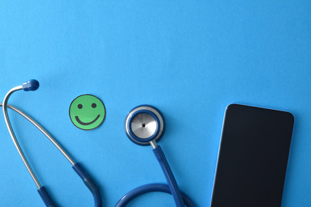 Online healthcare with smartphone, stethoscope and paper smiley face on blue background. Top view.の写真素材