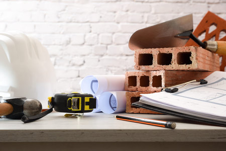 Architect's desk with plans and construction materials on white wooden table in office. Front view.