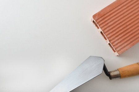 Masonry and construction trowel with metal trowel with wooden handle and brick with three orange holes isolated on white background.. Top view.の写真素材