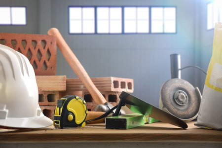 Construction materials such as trowel, bricks, cement and tools on a wooden board in an industrial...