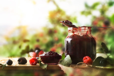 Natural berry jam in glass jar on wooden table with fruits and nature background. Front view.