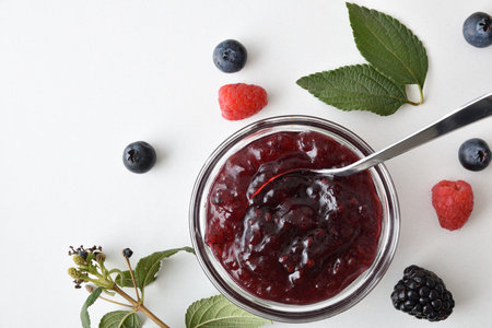 Detail of bowl with forest fruit jam isolated on white table with berries and leaves around. Top view.の写真素材