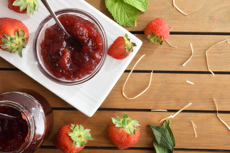Natural strawberry jam in glass jars on wooden table with fruits in nature. Top view.の写真素材