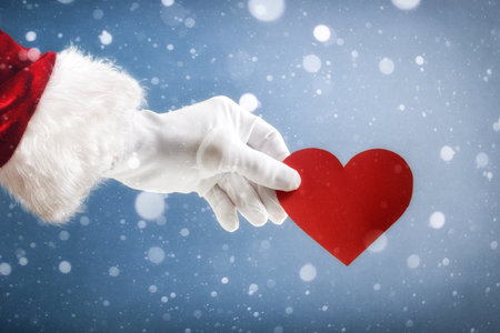 Christmas love concept with Santa Claus hand holding a heart cutout on snowy background.の写真素材