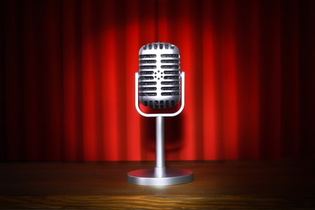 Vintage metal microphone with stand in the center of a stage with wooden platform and red curtains illuminated with a spotlight.の写真素材