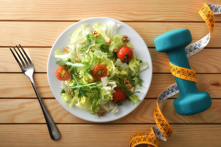 Healthy living and diet with plate with salad and fork on a wooden slatted table with a dumbbell and measuring tape. Top view.の写真素材