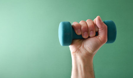 Hand holding blue neoprene dumbbell for muscle strengthening sport isolated on blue gradient...