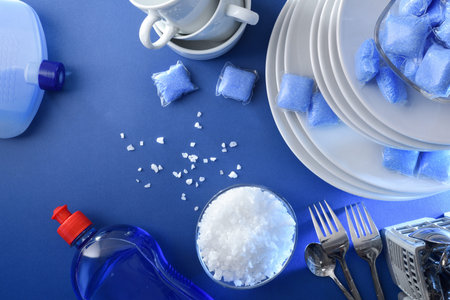 Detail of dishwasher products with cutlery, plates, cups and glasses on blue table. Top view.
