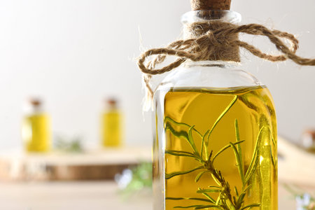 Detail of glass jar with rosemary oil and twigs inside on wooden table and isolated background....