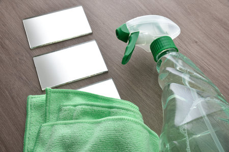 Cleaning product for dirt and dust in a transparent plastic bottle spray on wooden table with microfibre cloth and glass. Elevated view.の写真素材
