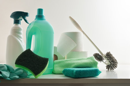 Bathroom cleaning supplies such as disinfectant bottles, scouring pads, gloves, toilet brush and toilet paper on white wooden cabinet with white isolated background. Front view.の写真素材