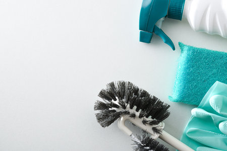 Detail of bathroom cleaning supplies such as disinfectant bottles, scouring pads, gloves, toilet brush and toilet paper isolated on white wooden table. Top view.の写真素材