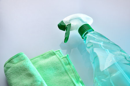 Multi-surface disinfectant cleaner in a clear plastic spray bottle and green microfiber cloth on a white reflective base. Elevated view.の写真素材