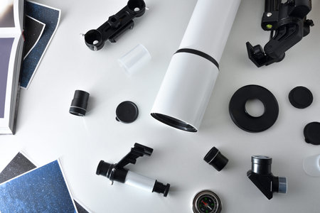 parts of a disassembled telescope on a white table with pictures and book. Top view.