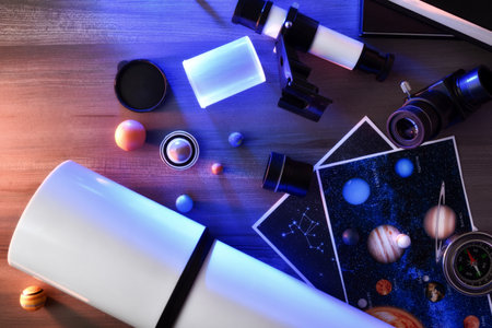 Telescope and telescope parts ready for space exploration on wooden table with books and photographs illuminated with red and blue lights. Top view.の写真素材