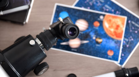 Concept of the study and exploration of planets with detail of the eyepiece of a student telescope with material, books and photographs on a wooden table. Top view.の写真素材