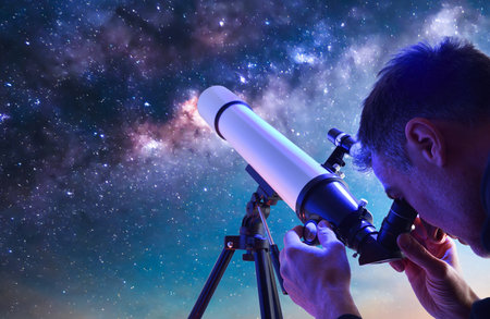 Detail of man outdoors looking through the eyepiece of a telescope focusing on a blue sky full of stars.の写真素材