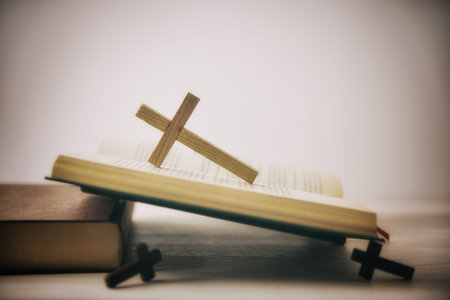 Old open Bible on a wooden table with several wooden crosses and isolated white background. Side...