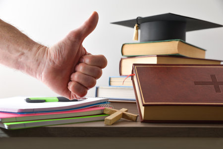 Wooden table full of educational material, books and Bible, and hand with OK gesture, isolated on white background. Concept of religious studies.の写真素材